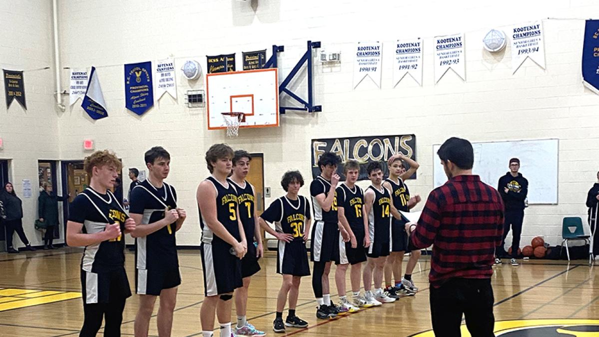 High school basketball players in black and yellow uniforms line up in a gymnasium to receive their medals. 