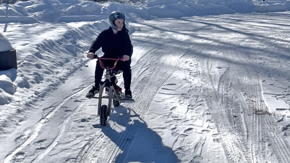 A high school student rides a mini-bike through a snowy parking lot. 