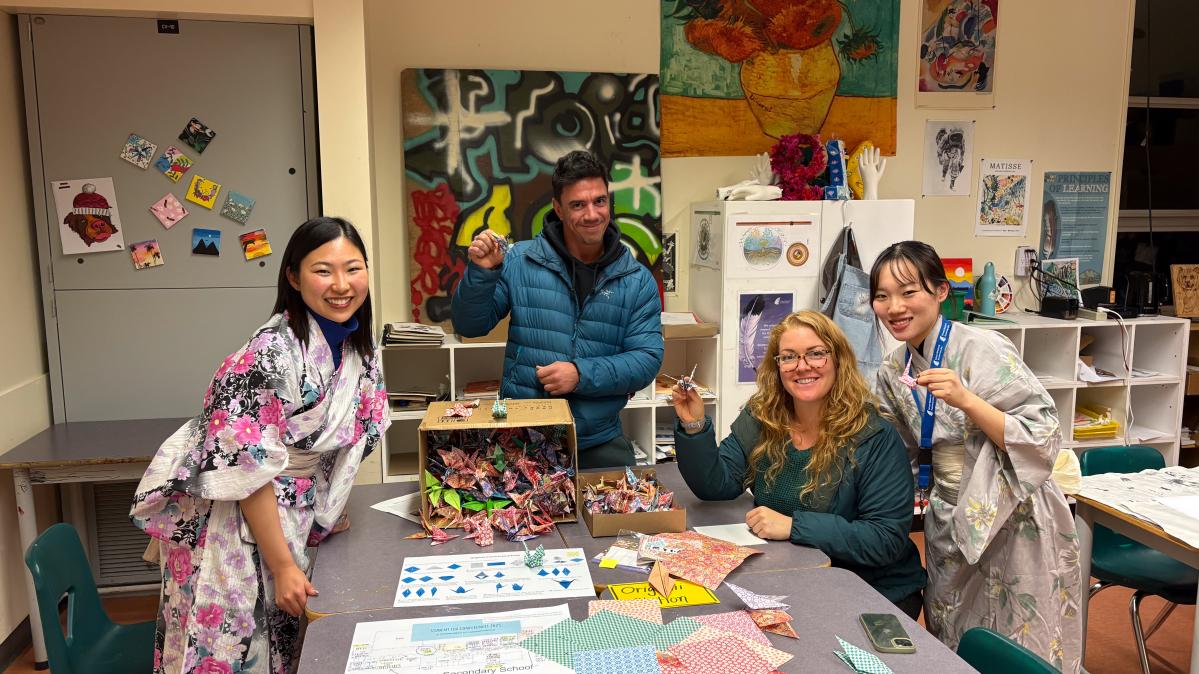 Two young women in Japanese kimono smile beside a middle aged women and man at a table in a school
