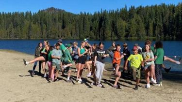 A group of youth in colourful clothing on a beach in front of a lake