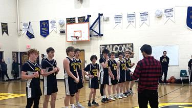 High school basketball players in black and yellow uniforms line up in a gymnasium to receive their medals. 