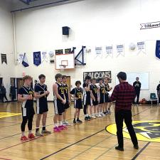 High school basketball players in black and yellow uniforms line up in a gymnasium to receive their medals. 