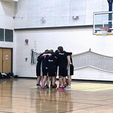 A group of highschool basketball players in a scrum before a game in a high school gymnasium.