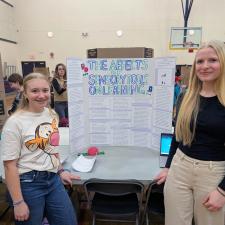 Two young woment beside a poster at a school science fair