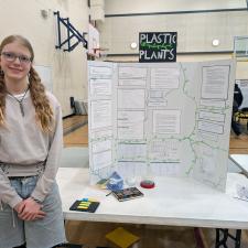 A young woman beside a poster at a school science fair