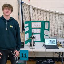 A young man beside a poster at a school science fair