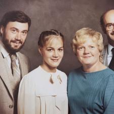 A young man and woman in formal dress pose beside their parents in a family portrait from the 1970s